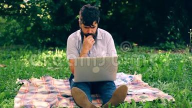 一个留胡子的人在公园里拿着笔记本电脑。